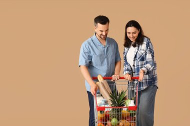 Bej arka planda alışveriş arabası olan genç ve güzel bir çift.