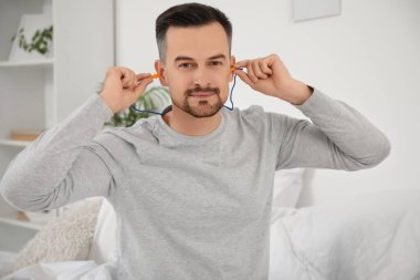 Yakışıklı adam yatak odasına kulak tıkacı koyuyor.