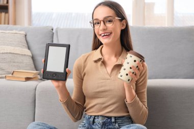 Evde e-okuyucusu ve kahvesi olan genç bir kız.