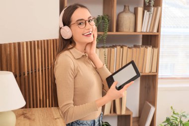 Kulaklıklı genç kız evde e-kitap okuyor.