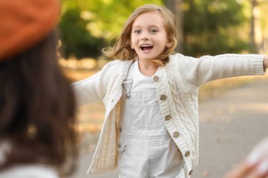 Mutlu kız, güzel sonbahar parkında koşarken ailesine sarılmak için kollarını açıyor.