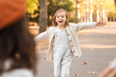 Mutlu kız, güzel sonbahar parkında koşarken ailesine sarılmak için kollarını açıyor.