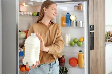 Mutfaktaki açık buzdolabının yanında bozuk sütü olan genç bir kadın.