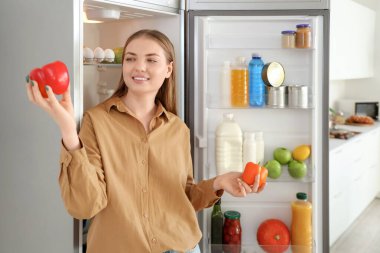 Mutfaktaki açık buzdolabının yanında biberli genç bir kadın.