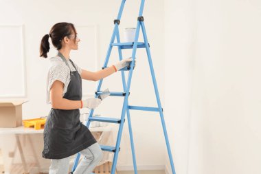 Odadaki merdiven üzerinde macun bıçağı olan kadın işçi.