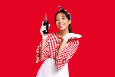 Kırmızı arka planda bir şişe sodayla gülümseyen genç Asyalı garson.