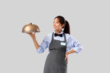 Genç Asyalı gülümseyen garson tepsisi ve gri arka planı ile