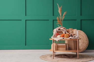 Sonbahar dekorasyonlu kahve masası, bir fincan çay, iplik ve yeşil duvarın yanında kitaplar.