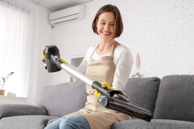 Evdeki koltukta oturan modern elektrikli süpürgeyle güzel bir genç kadın.