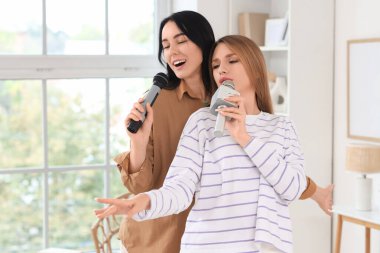Evde mikrofonlu güzel genç kadınlar karaoke yapıyor.