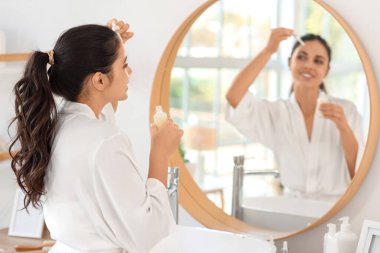 Güzel, genç, mutlu bir kadın banyoda aynanın yanında kozmetik yağı sürüyor.