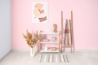 Raflar, merdiven, vazodaki otlar ve odadaki pembe duvarda resim.