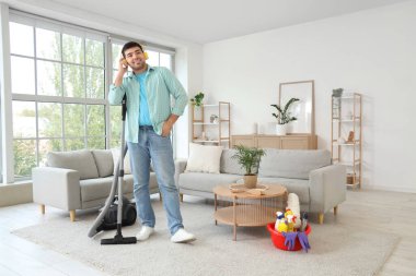 Halıyı süpüren ve odada müzik dinleyen genç bir adam.