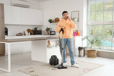 Genç adam evini temizlerken telefonla konuşuyor.