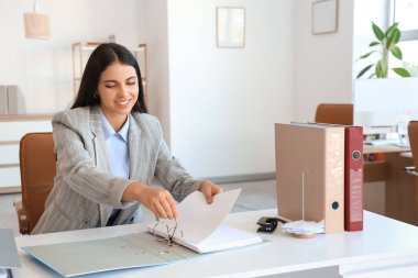 Ofiste belgelerle çalışan genç bir iş kadını.