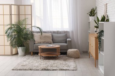 Oturma odasının içinde kanepe, katlanan ekran ve pencerenin yanındaki masa.