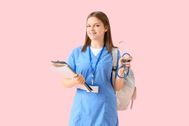 Pembe arka planda not defteri ve steteskobu olan bir tıp öğrencisi.