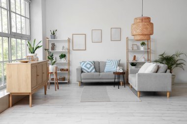 Gri kanepeler, raf üniteleri ve bitkilerle aydınlık oturma odasının içinde.