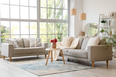 Oturma odasının içinde gri koltuklar ve vazoda şakayık çiçekleri var.