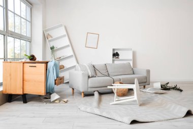 Depremden sonra kanepe, çekmece ve raf üniteleriyle dolu dağınık bir oturma odası.