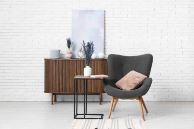 Dekorlu ahşap dolap, poster, lavanta çiçekleri ve hafif tuğla duvarın yanındaki rahat koltuk.