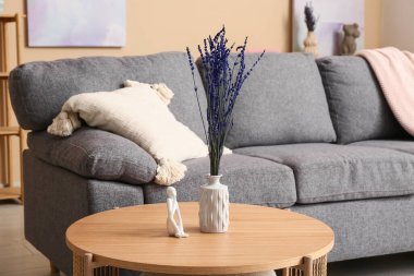 Ahşap masa, lavanta çiçekleri, dekor ve oturma odasında rahat bir kanepe.