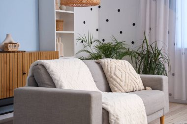 Gri kanepesi, palmiye ağaçları ve raf ünitesi olan oturma odasının içinde.