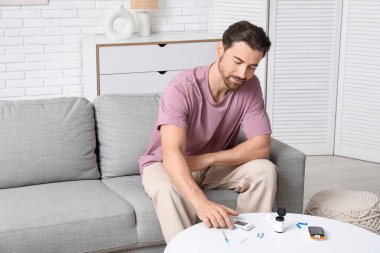 Diyabetli genç adam evde masadan glukometre alıyor.