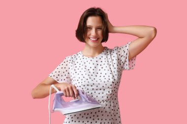 Pembe arka planda demir tutan gülümseyen genç kadın.