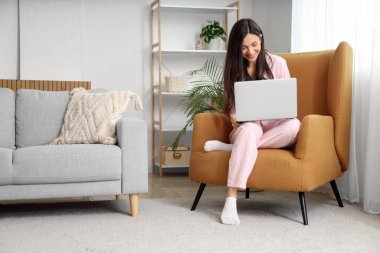 Evde dizüstü bilgisayarla çalışan pembe pijamalı serbest çalışan bir kadın.