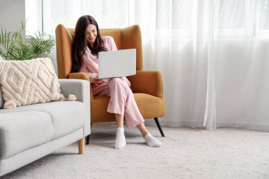 Evde dizüstü bilgisayarla çalışan pembe pijamalı serbest çalışan bir kadın.