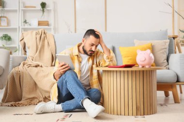 Evde para sayan tabletli stresli bir genç adam.