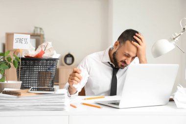 Ofisinde buruşmuş kağıtlarla stresli bir iş adamı