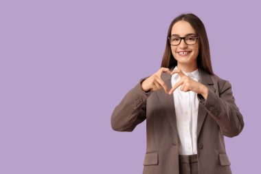 Güzel genç bir kadın parmaklarıyla leylak arka planda kalp yapıyor.