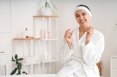 Güzel genç bir kadın banyoda duştan sonra dudak kremi sürüyor.