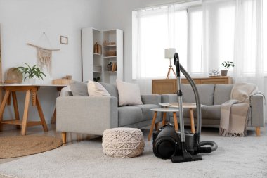 Elektrik süpürgesi, kanepe ve masalarla aydınlık oturma odasının içinde.