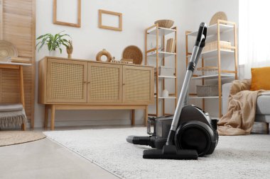 Elektrik süpürgesi, çekmeceler ve raf üniteleriyle aydınlık oturma odasının içinde.