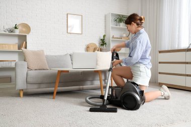 Oturma odasında elektrikli süpürgesi olan genç bir kadın.