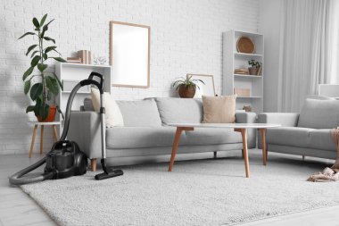 Oturma odasının içinde elektrikli süpürge, kanepe ve raf üniteleri var.