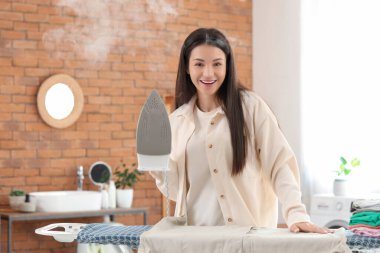 Güzel, genç ve mutlu bir kadın banyoda demir ve kıyafetlerle.