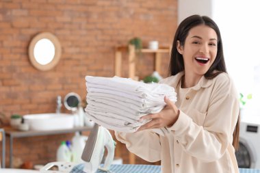 Güzel, genç, mutlu bir kadın. Banyoda bir yığın beyaz elbise ve ütüyle.