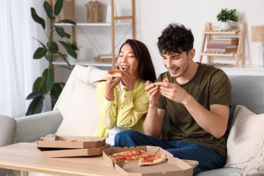 Evdeki kanepede pizza yiyen genç bir çift.