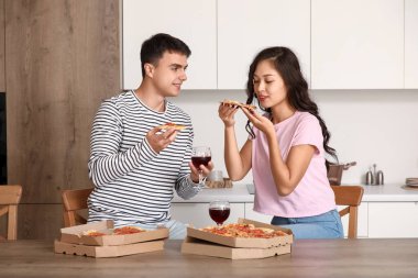 Şarabı olan genç bir çift mutfakta pepperoni pizza yiyor.