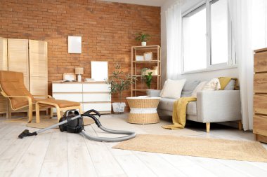 Oturma odasının içinde elektrikli süpürge, kanepe ve koltuk var.