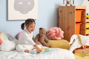 Pijamalı şirin küçük kız çocuk odasında yatakta eğitici oyuncaklarla oynuyor.