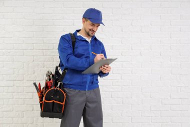 Beyaz tuğla arka planda panoya yazı yazan bir çanta dolusu aleti olan erkek teknisyen