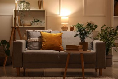 Yumuşak kanepe, sehpa ve gece oturma odasının içinde parlayan lamba.