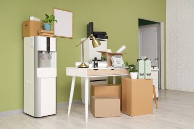 Taşınma gününde iş yerindeki yeşil duvarın yanında su soğutucusu ve karton kutuların olduğu yer.