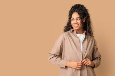 Güzel bir Afro-Amerikalı kadın, bej arka planda şık bir gömlek ilikliyor.