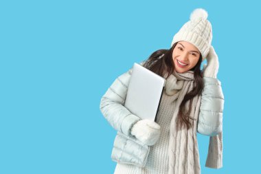 Mavi arka planda dizüstü bilgisayarı olan kışlık elbiseli genç bir kadın.